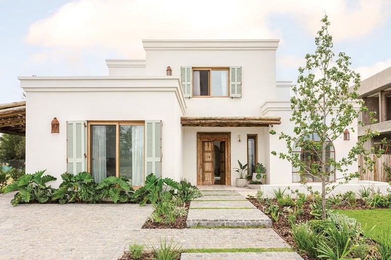 Modern two-story white house with wooden entrance door, shutters, front paver driveway, landscaped garden, and climbing ivy on right side